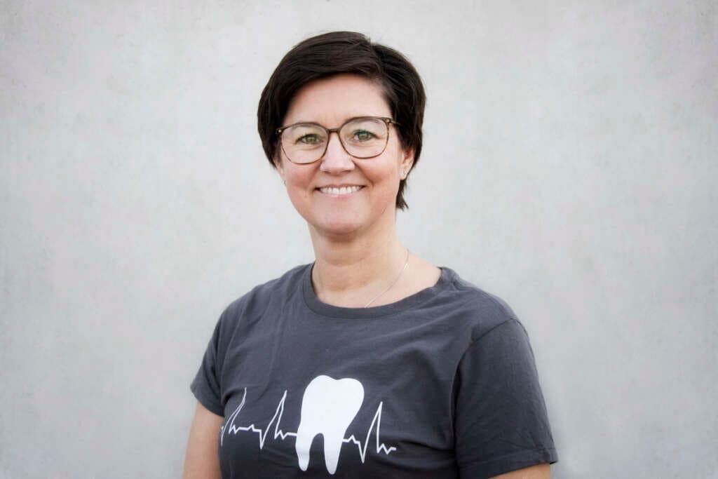 Teammitglied mit Brille und Zahn-Shirt vor grauer Wand
